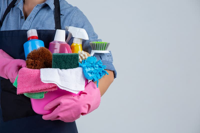 Junge Frau hält Reinigungsmittel in der Hand mit Gummihandschuhen.